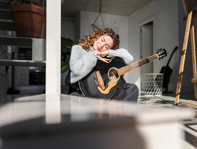 woman sitting on floor holding black acoustic guitar in bright room with plants and natural light enjoying music and relaxation 2 acoustic melodies 2 moments