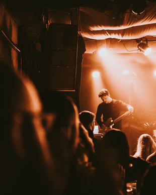 man playing guitar on stage in a dimly lit venue with audience watching live music performance at night three musicians in a band