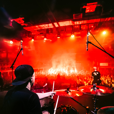 drummer performing on stage with vibrant lights and enthusiastic crowd during concert 13th performance event