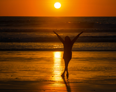 silhouette of a person with arms raised at sunset over the ocean reflecting golden light serene beach moment with two waves