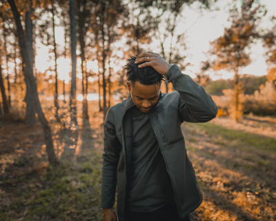 man in a black jacket touching his hair standing in a forest during sunset showcasing style and confidence outdoor fashion 1