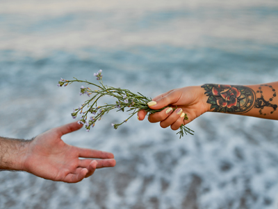 hands exchanging flowers at the beach with a tattoo showcasing nature and connection 1 gifts and nature