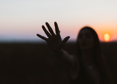 silhouette of a woman reaching out against a sunset backdrop featuring two fingers raised as a gesture of peace and connection